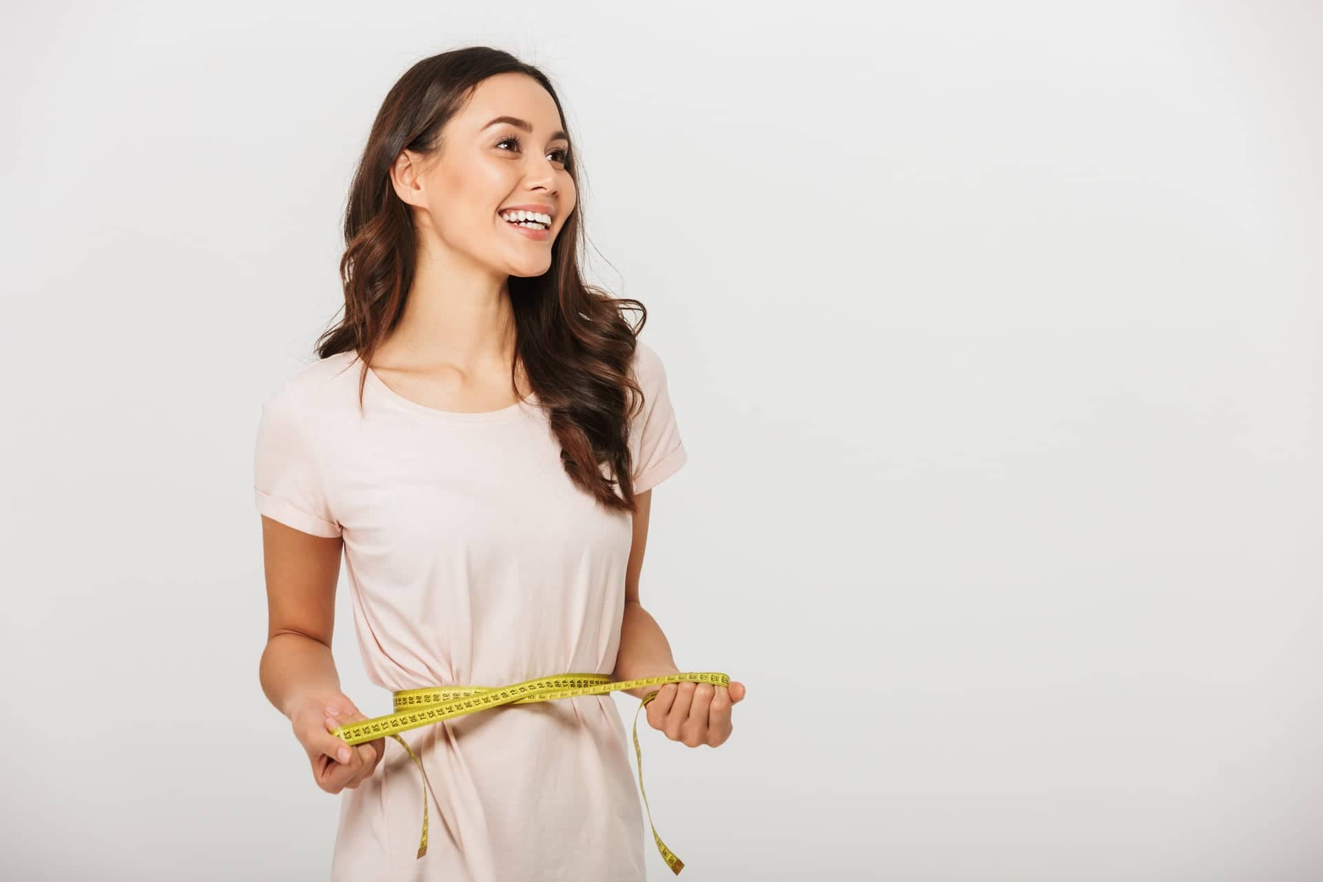 Redukce hmotnosti – usmívající se žena měří obvod pasu krejčovským metrem